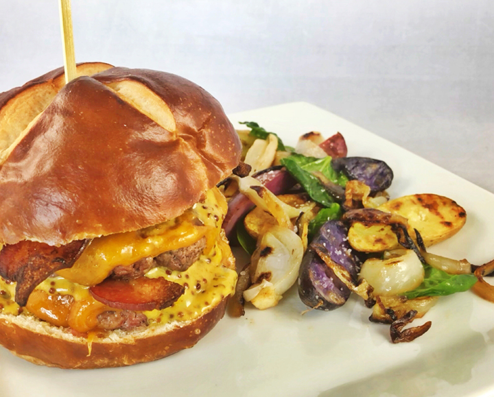 Pretzel Bun Burger with Cheddar, Bacon, Spicy Mustard Sauce, and Grilled Fingerling Potatoes & Onions